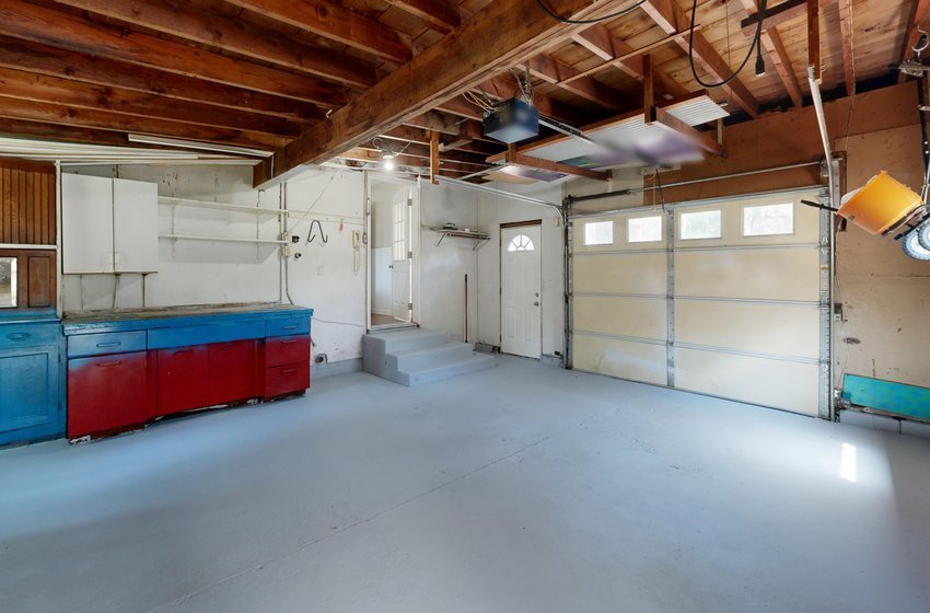 An empty garage with a clean concrete floor, painted cabinets and a closed garage door