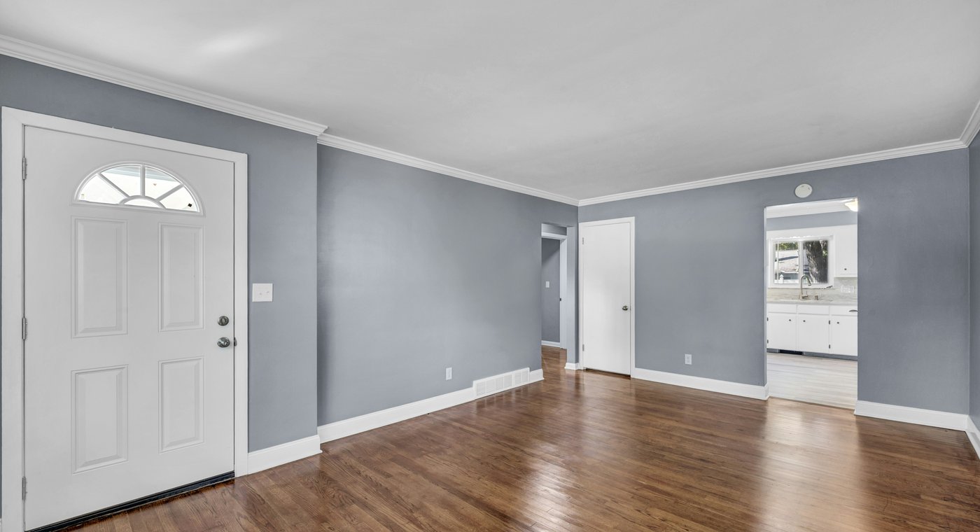 An empty living room with gray walls, white trim and hardwood floors after everything was cleared out