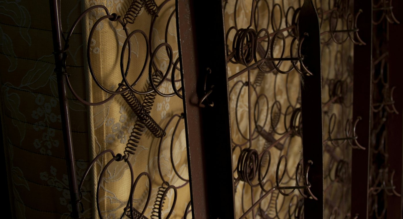 Old coil-spring mattresses and box springs standing on edge, the coils showing through the fabric