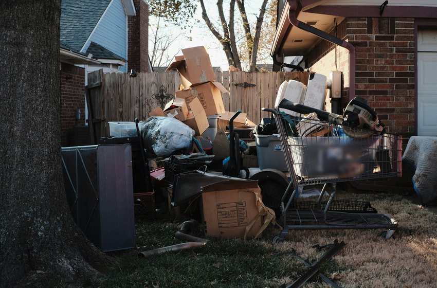A pile of boxes, plastic bins and old tools on the lawn beside a brick house